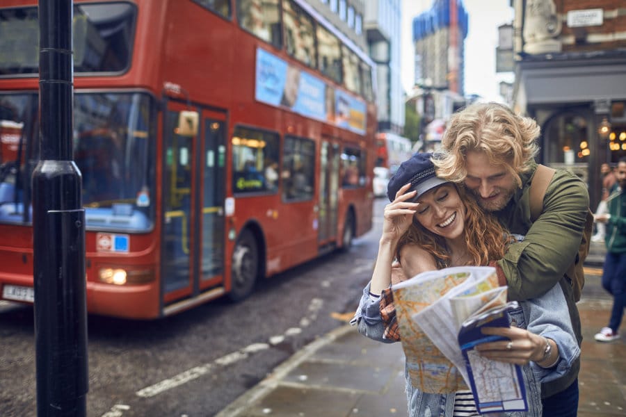 Ein Paar macht eine Städtereise in London, steht am Strassenrand und blickt in einen Stadtplan Europa