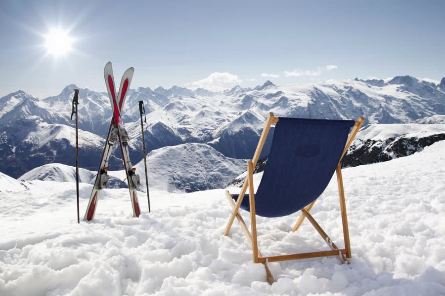 Dies ist das Kategoriebild Skiurlaub und verlinkt auf die Unterseite Winterurlaub und Skiurlaub in Österreich. Ein Klappliegestuhl steht im Schnee, man sieht Skier und eine Panoramaaussicht auf die umliegenden, verschneiten Berge.